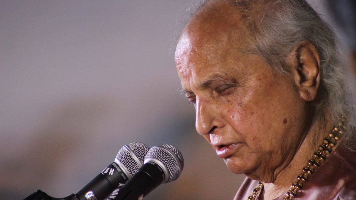 Pandit Jasraj with white hair, eyes closed, singing at microphones