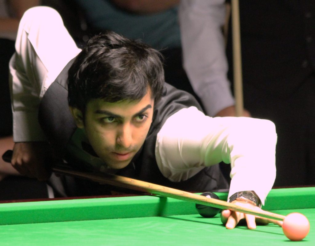Pankaj Advani leaning over a snooker table, lining up a shot with his cue
