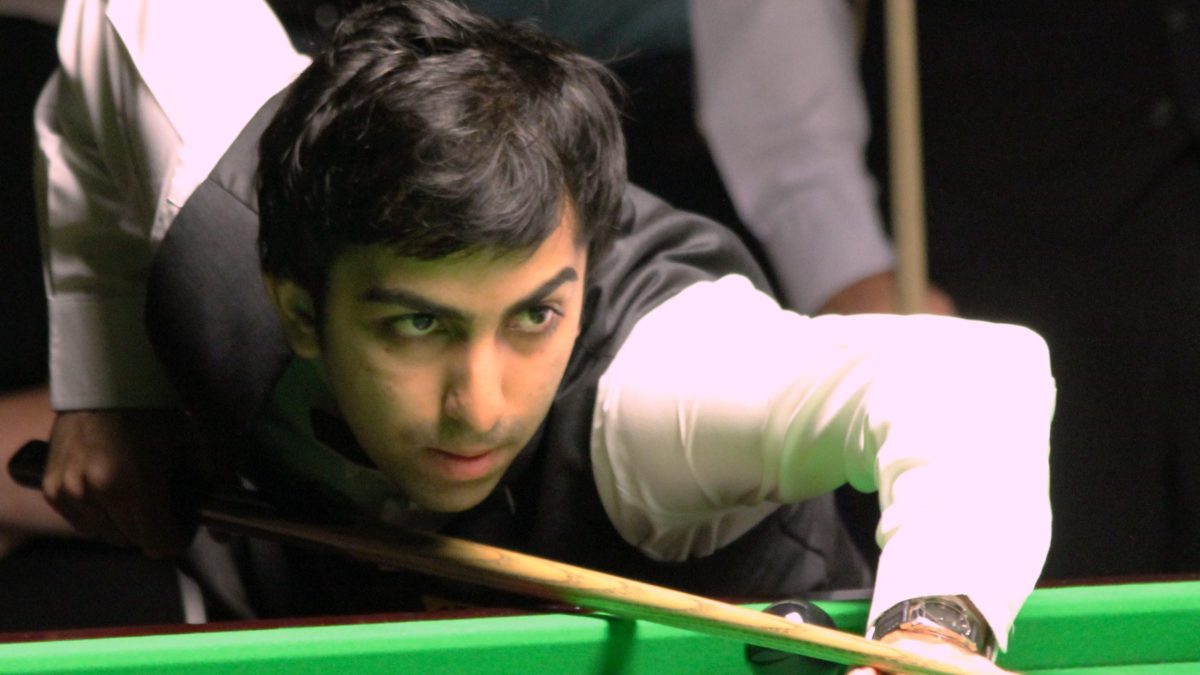 Pankaj Advani leaning over a snooker table, lining up a shot with his cue