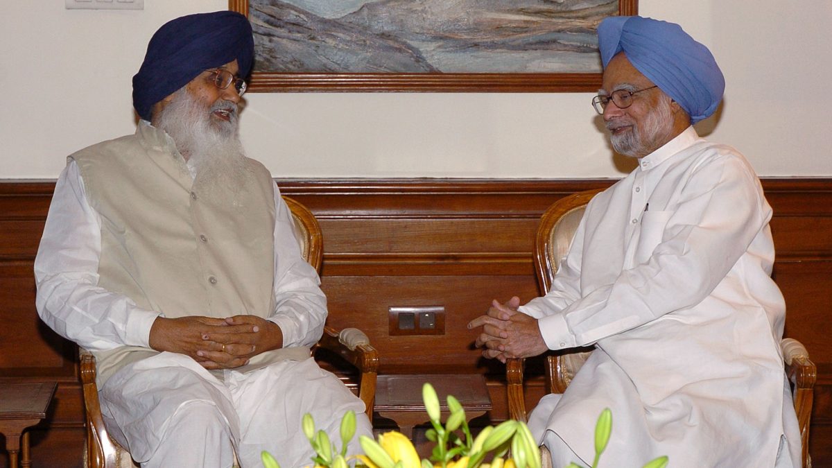 Parkash Singh Badal with a white beard and turban seated in conversation with Prime Minister Manmohan Singh