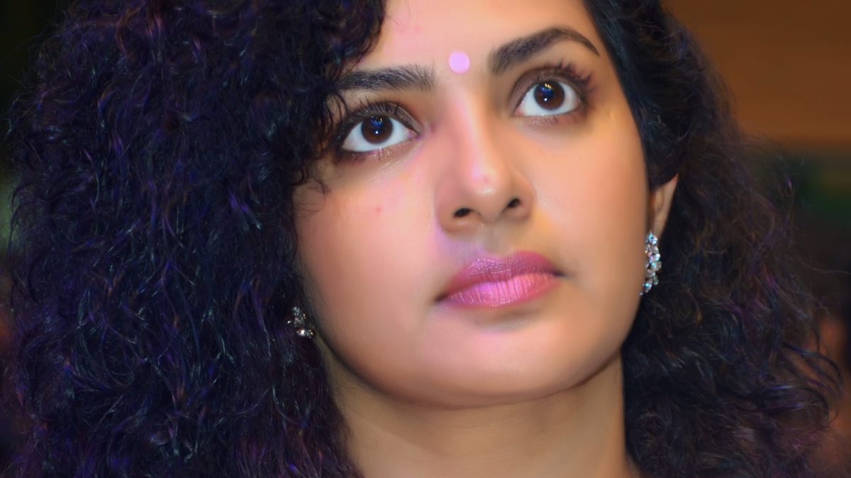 Parvathy Thiruvothu with curly hair, looking upward, in a pale sari