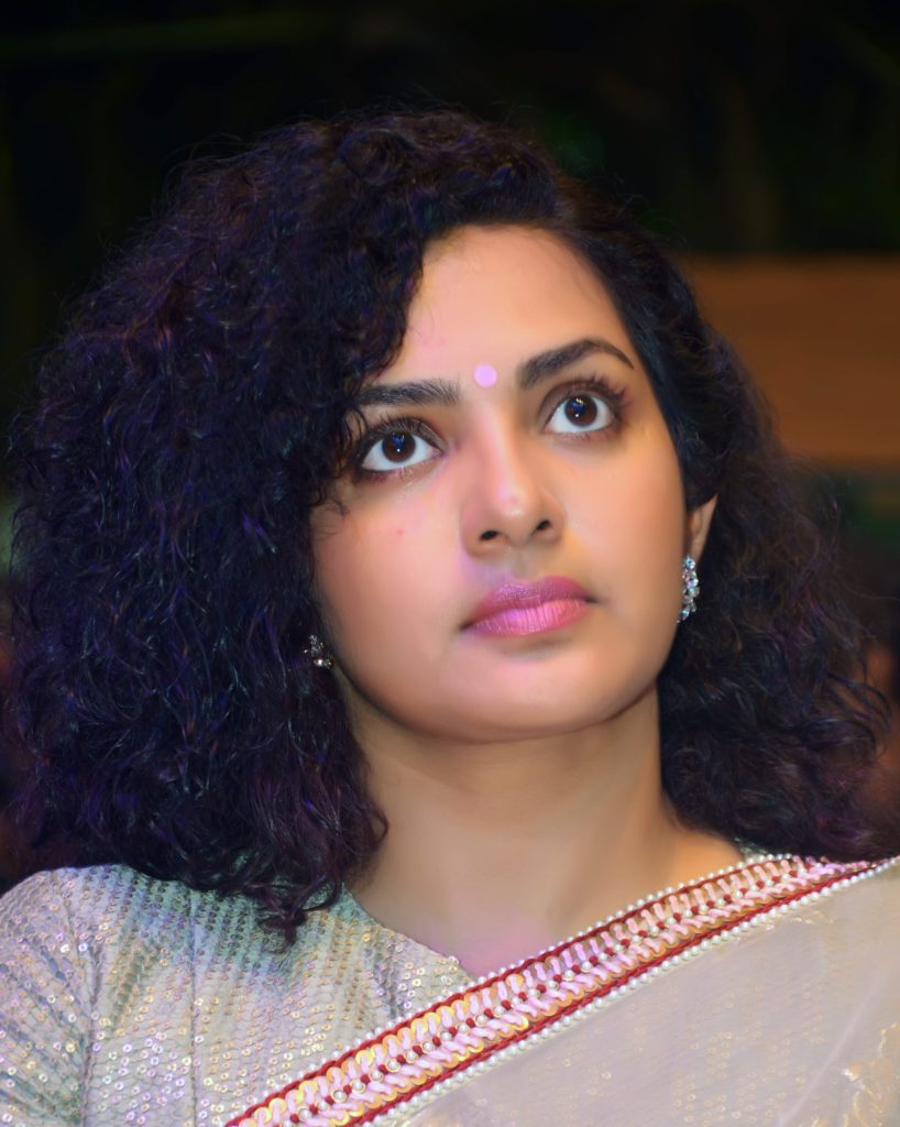 Parvathy Thiruvothu with curly hair, looking upward, in a pale sari