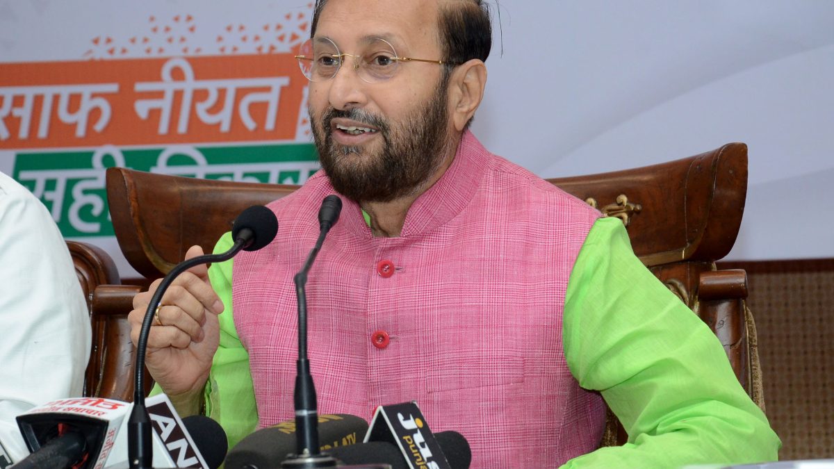 Prakash Javadekar in a pink kurta and green jacket speaking at press microphones