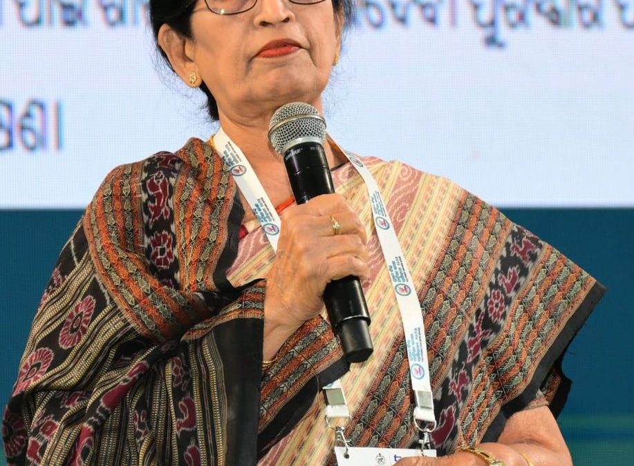 Pratibha Ray in a patterned sari speaking into a microphone on a stage