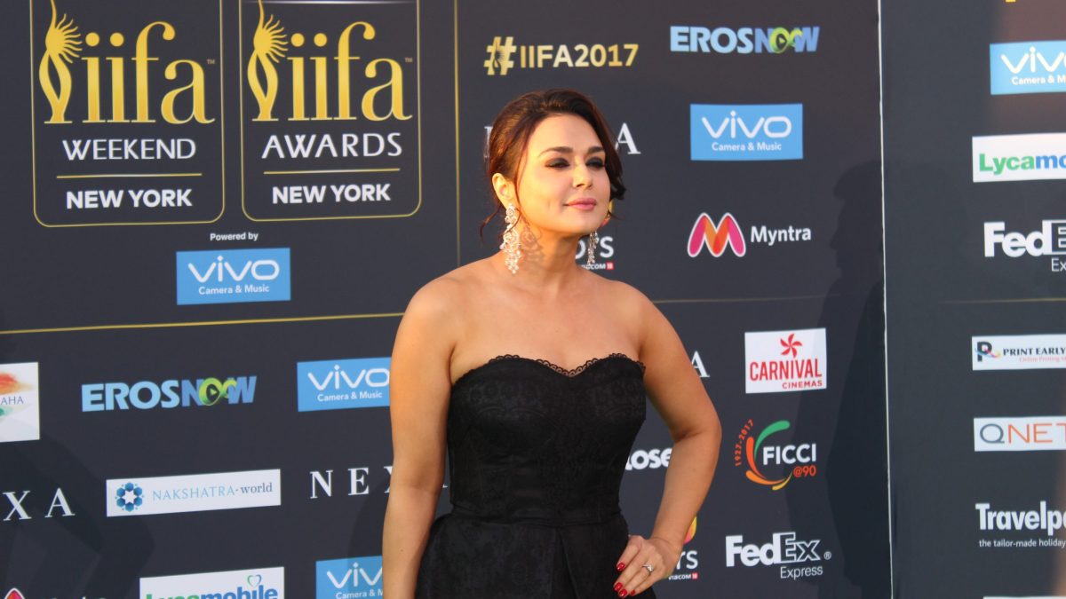 Preity Zinta in a black strapless dress posing in front of the IIFA sponsor wall