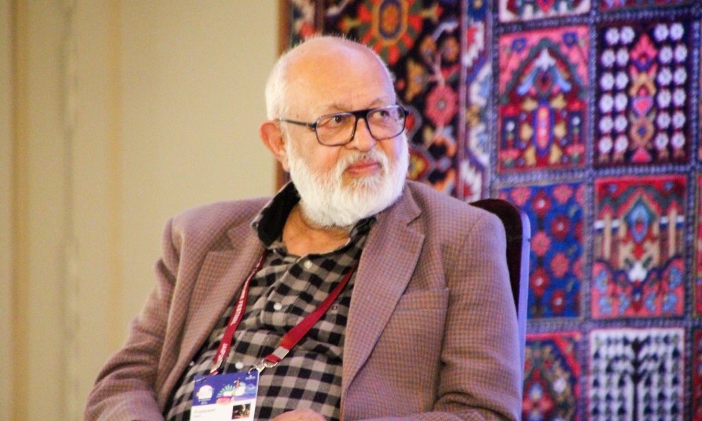 Pushpesh Pant with a white beard and glasses, in a checked jacket, seated at a festival