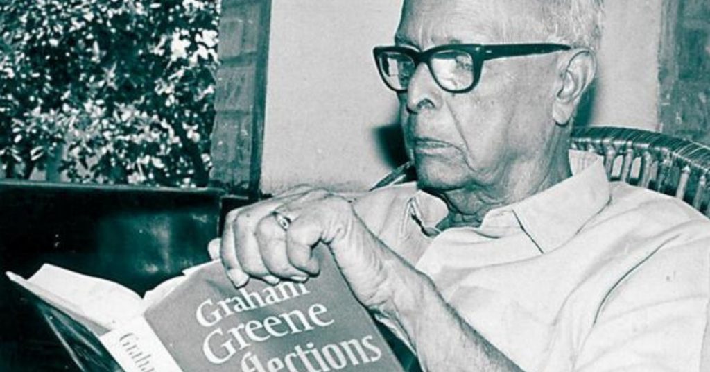 R. K. Narayan in glasses reading a book by Graham Greene