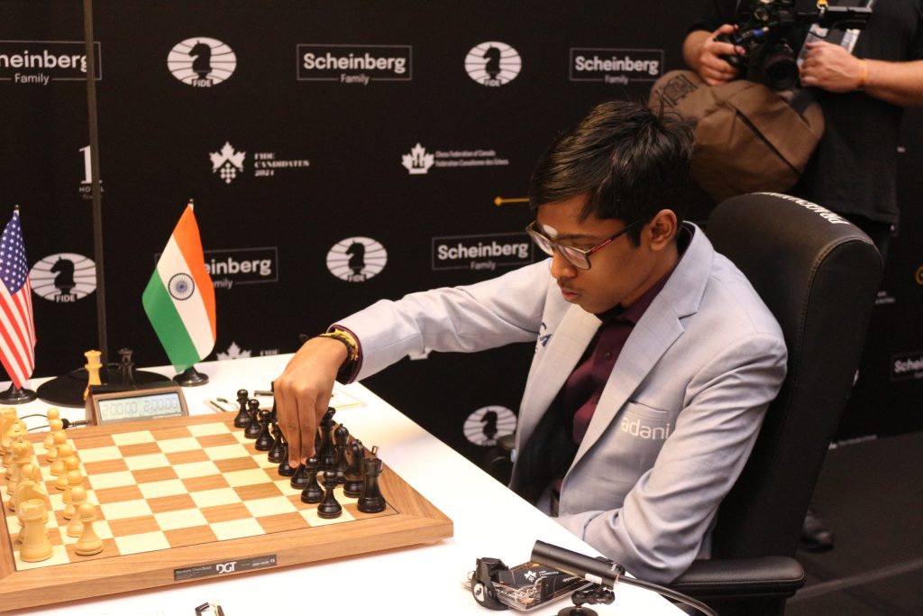 R. Praggnanandhaa in a grey suit making a move at a chessboard beside an Indian flag