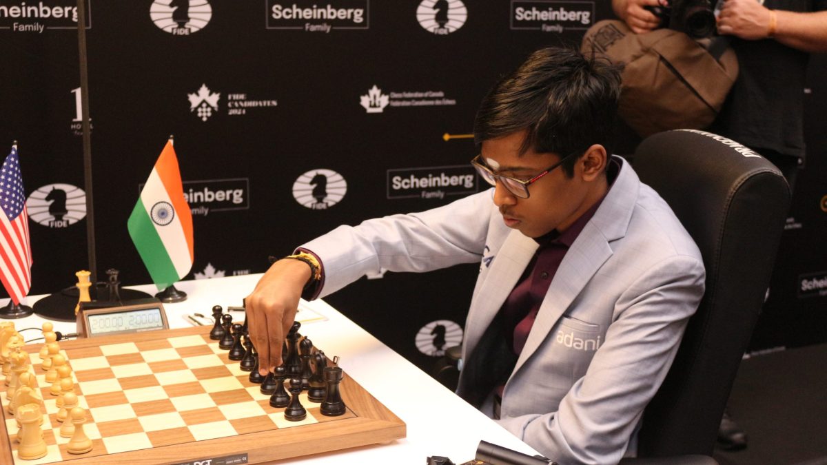 R. Praggnanandhaa in a grey suit making a move at a chessboard beside an Indian flag
