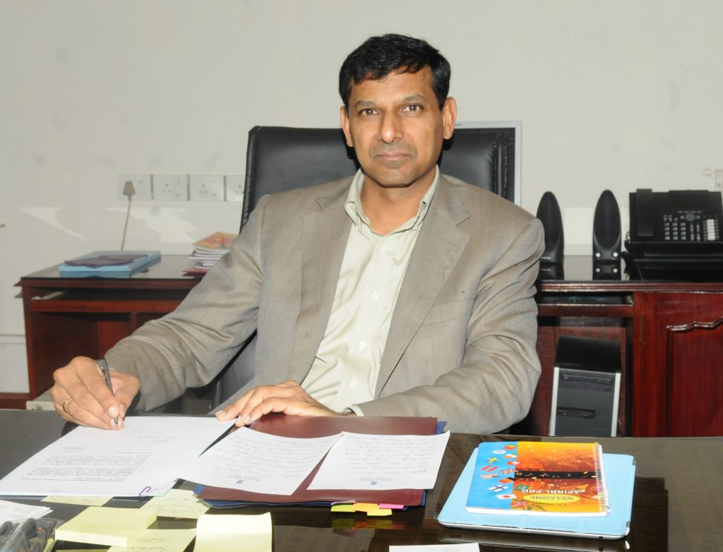 Raghuram Rajan in a light jacket signing papers at his desk