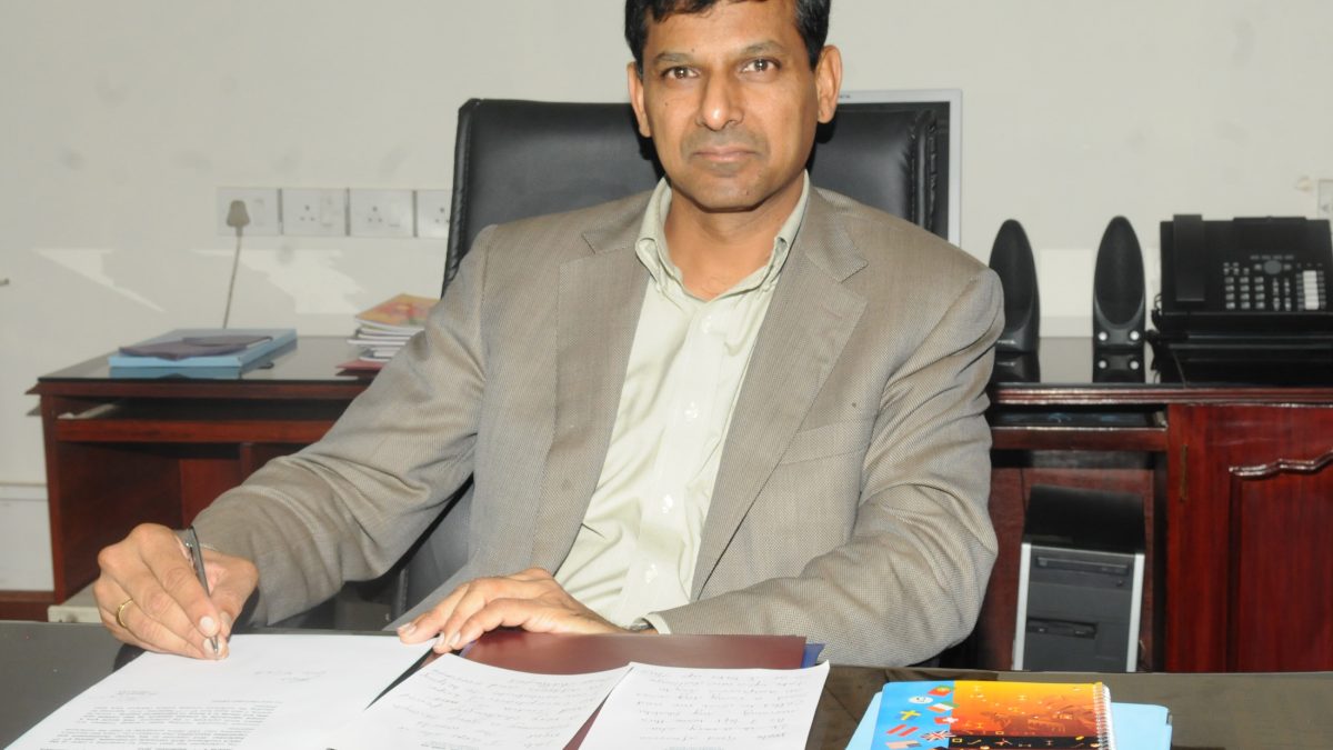 Raghuram Rajan in a light jacket signing papers at his desk
