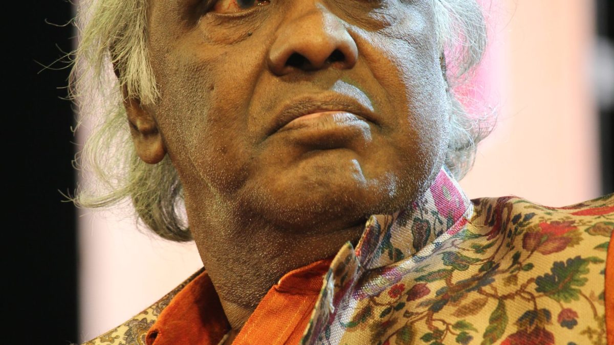 Rahat Indori seated at an event in an orange kurta and floral jacket