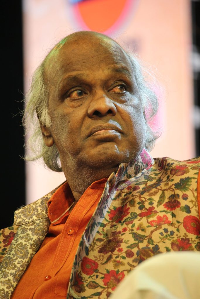 Rahat Indori seated at an event in an orange kurta and floral jacket
