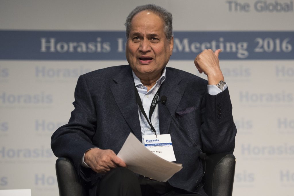 Rahul Bajaj with white hair in a dark suit seated on stage, gesturing as he speaks