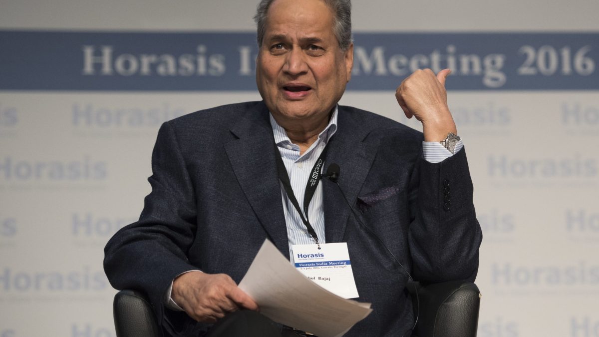 Rahul Bajaj with white hair in a dark suit seated on stage, gesturing as he speaks