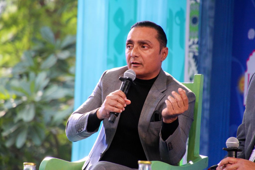 Rahul Bose in a grey blazer gesturing as he speaks into a microphone