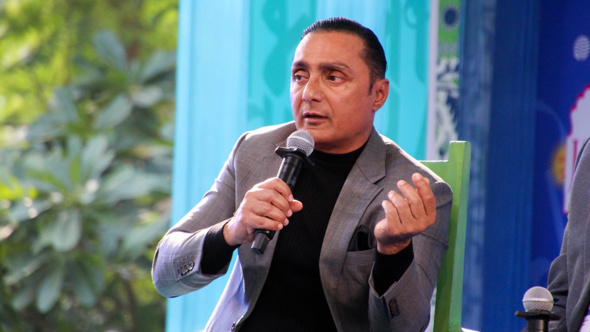 Rahul Bose in a grey blazer gesturing as he speaks into a microphone