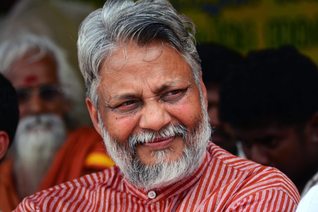 Close-up of Rajendra Singh with grey hair and beard, smiling in a striped red kurta