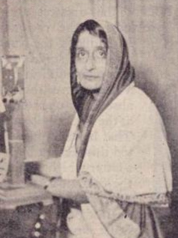 An old photograph of Rajkumari Amrit Kaur with her head covered, seated at a desk