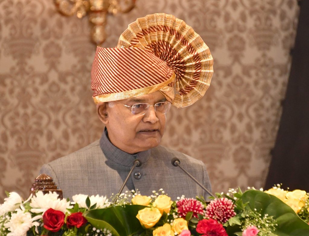 Ram Nath Kovind wearing a traditional turban, speaking at a podium decorated with flowers