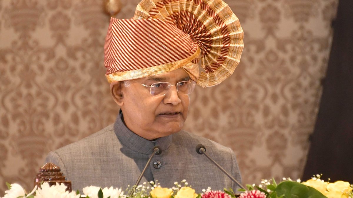 Ram Nath Kovind wearing a traditional turban, speaking at a podium decorated with flowers