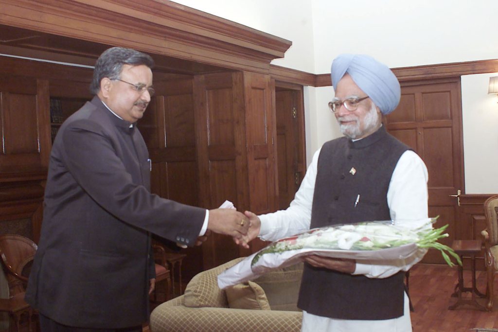 Raman Singh in a dark suit shaking hands with Prime Minister Manmohan Singh
