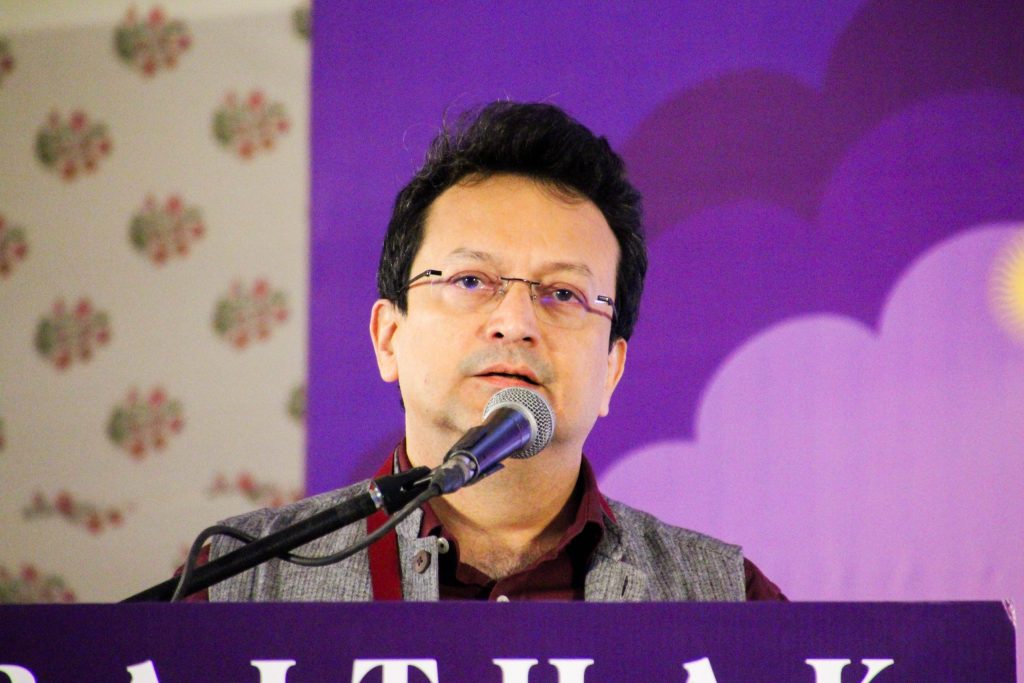 Ranjit Hoskote in glasses and a dark kurta speaking into a microphone
