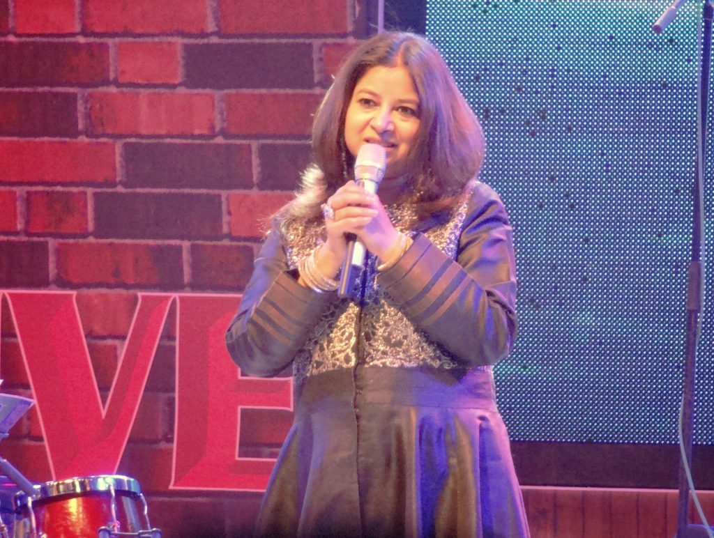 Rekha Bhardwaj in a purple outfit singing into a microphone on stage
