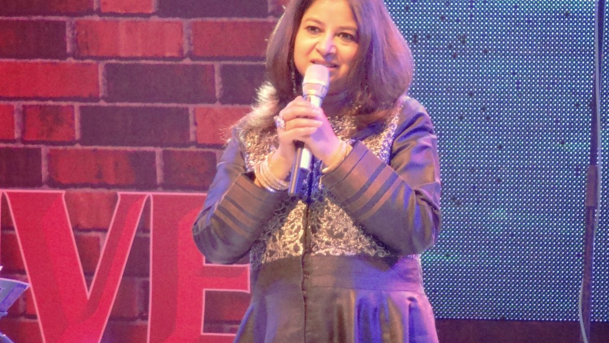 Rekha Bhardwaj in a purple outfit singing into a microphone on stage