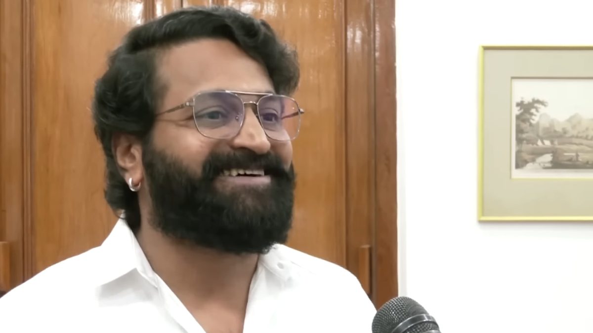 Rishab Shetty with a full beard, in a white shirt, smiling