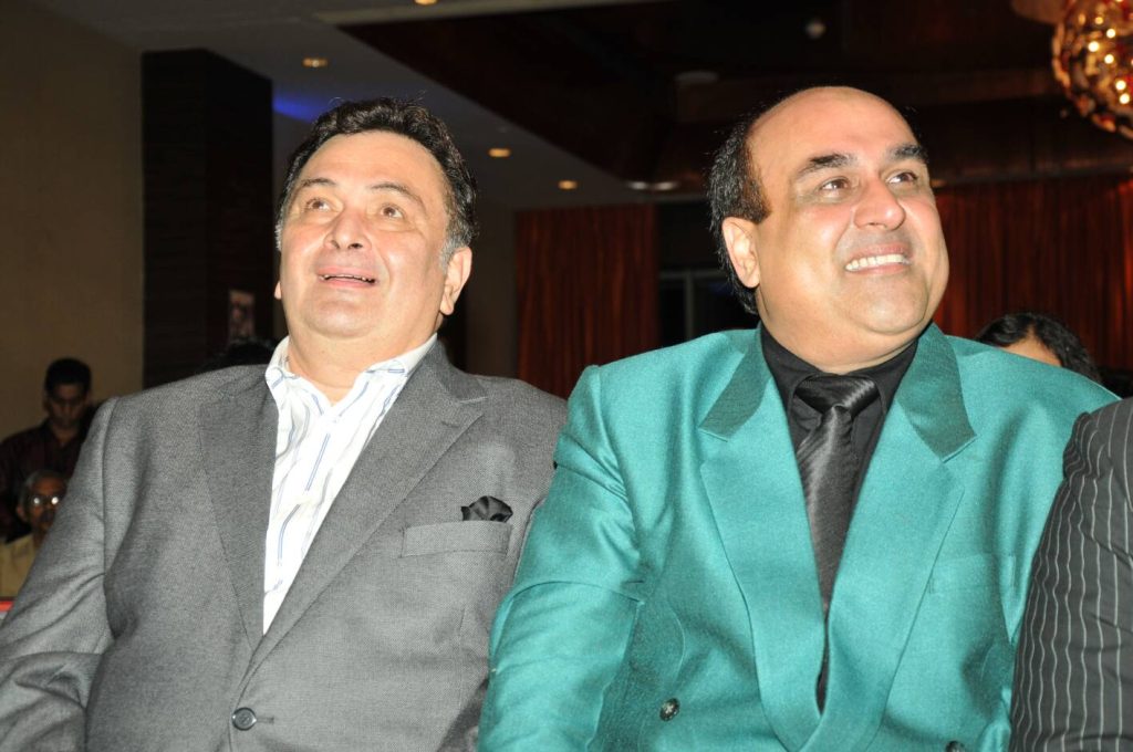 Rishi Kapoor in a grey suit smiling beside Shahid Rafi