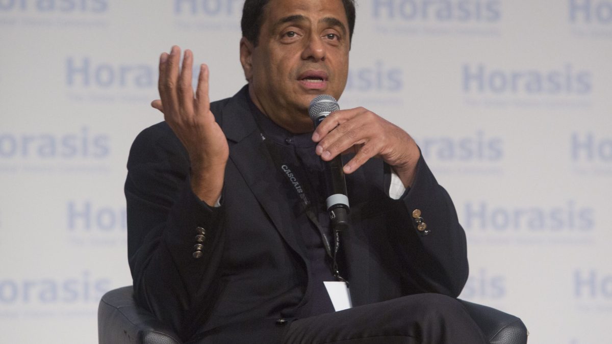 Ronnie Screwvala in a dark jacket seated on stage, gesturing with both hands