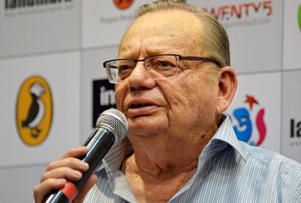 Ruskin Bond in glasses and a striped shirt speaking into a microphone