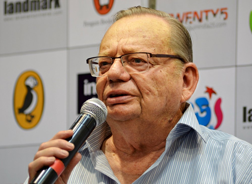 Ruskin Bond in glasses and a striped shirt speaking into a microphone