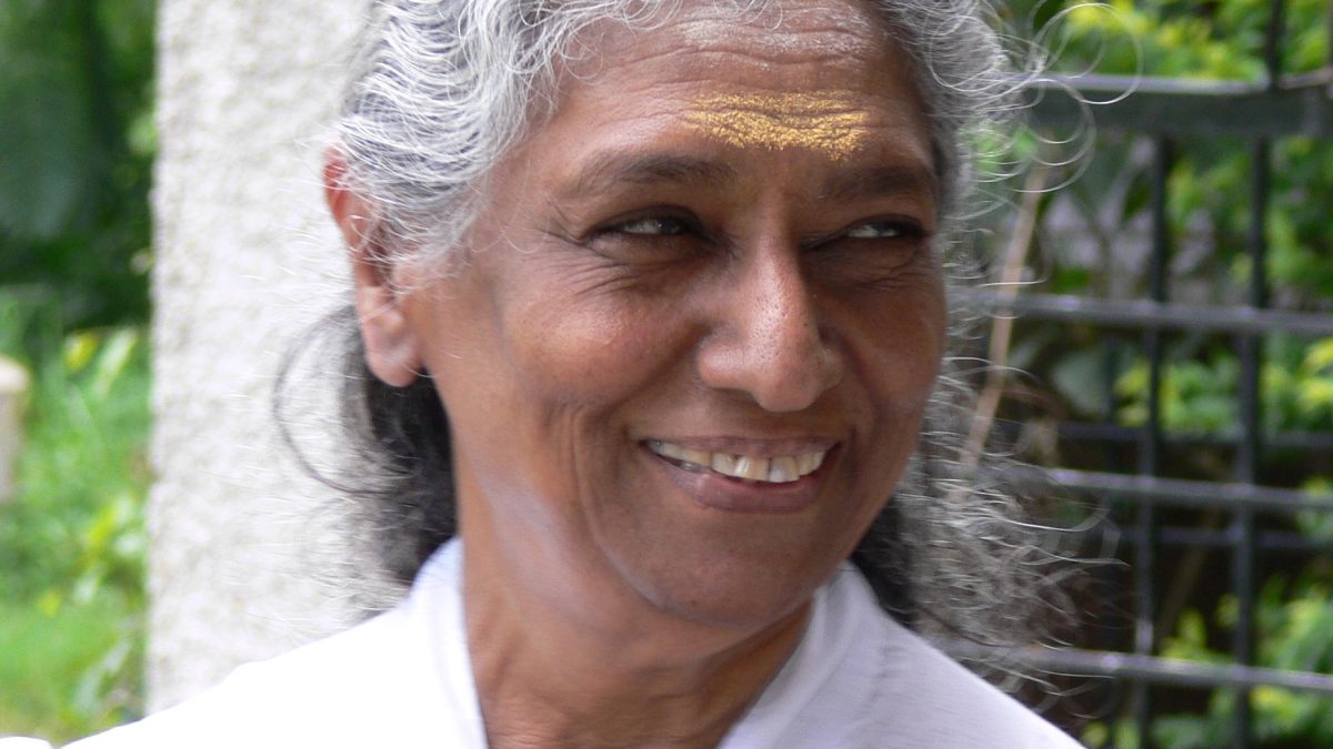 S. Janaki with white hair, smiling, in a white sari with a red border