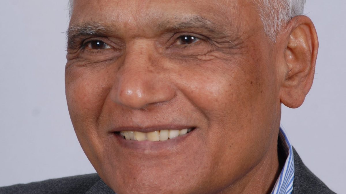S. L. Bhyrappa with white hair, smiling, in a dark jacket and striped shirt