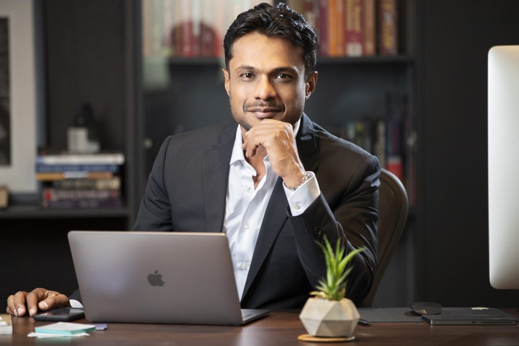 Sachin Bansal in a dark blazer seated at a desk with a laptop, hand to his chin