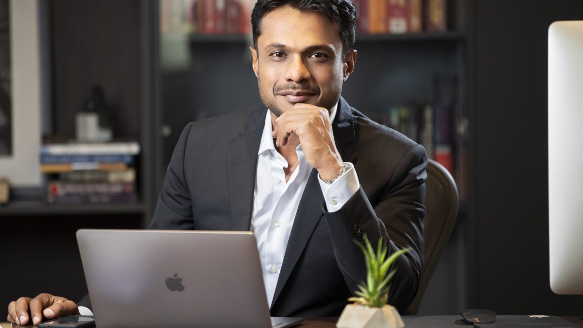 Sachin Bansal in a dark blazer seated at a desk with a laptop, hand to his chin