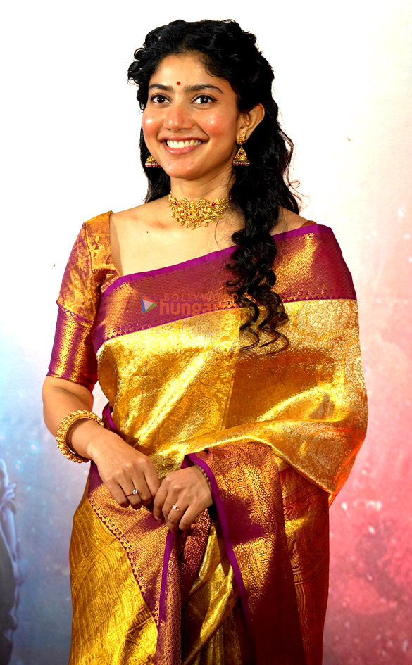 Sai Pallavi in a gold silk saree smiling at a Ramayana event