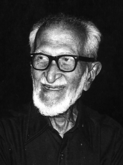 A black-and-white portrait of an elderly Salim Ali with a white beard and thick glasses