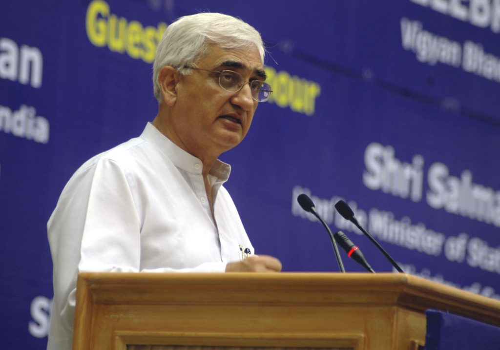 Salman Khurshid in a white kurta and glasses speaking at a lectern