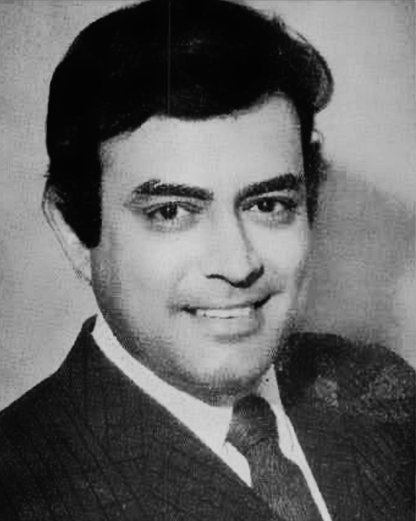 A black-and-white portrait of Sanjeev Kumar in a suit, smiling