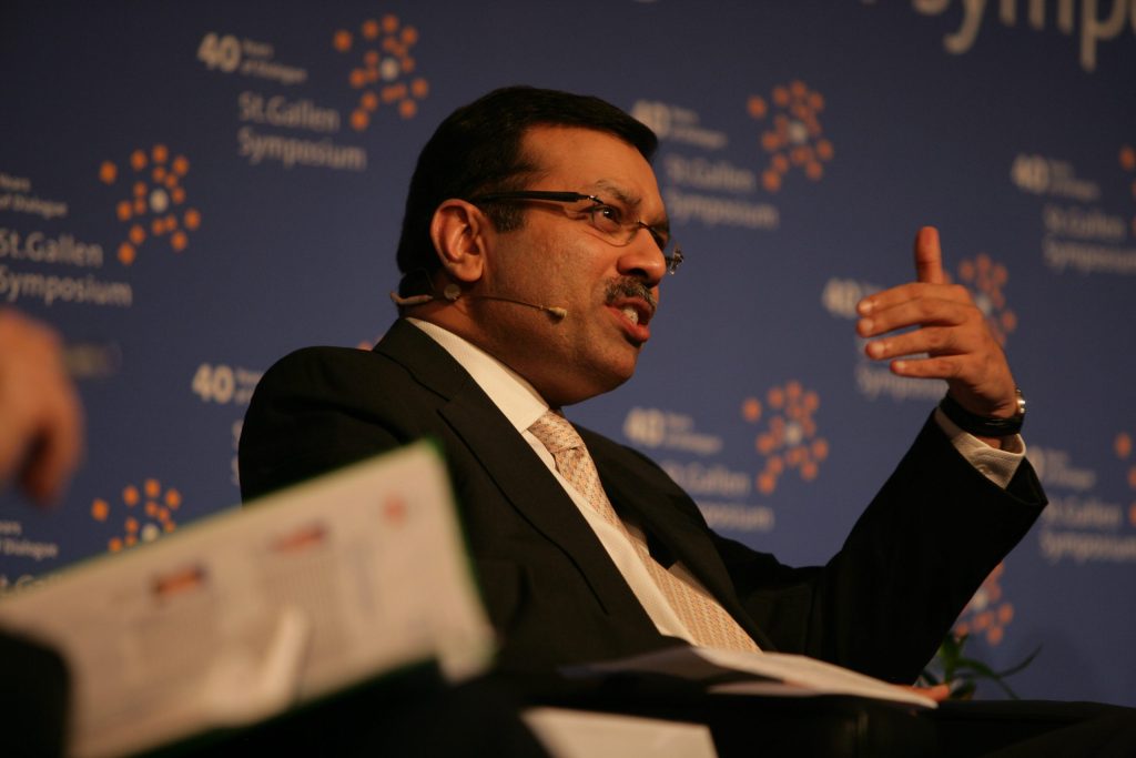 Sanjiv Goenka in glasses and a dark suit gesturing as he speaks on stage