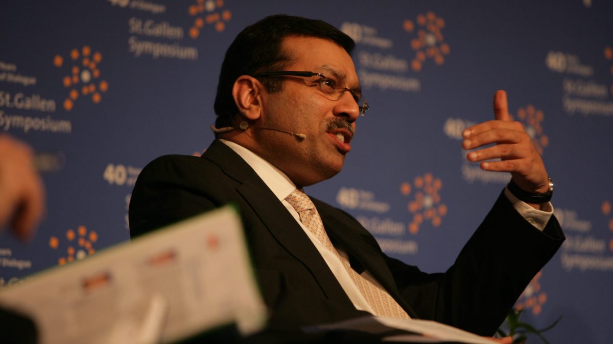 Sanjiv Goenka in glasses and a dark suit gesturing as he speaks on stage