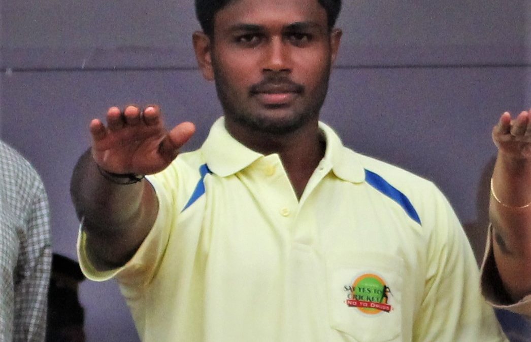 Sanju Samson in a yellow Kerala jersey raising his hand in a huddle