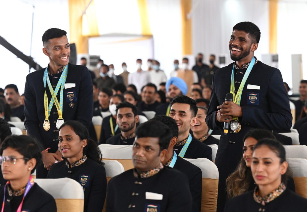 Satwiksairaj Rankireddy and Chirag Shetty standing and smiling with their medals among seated athletes