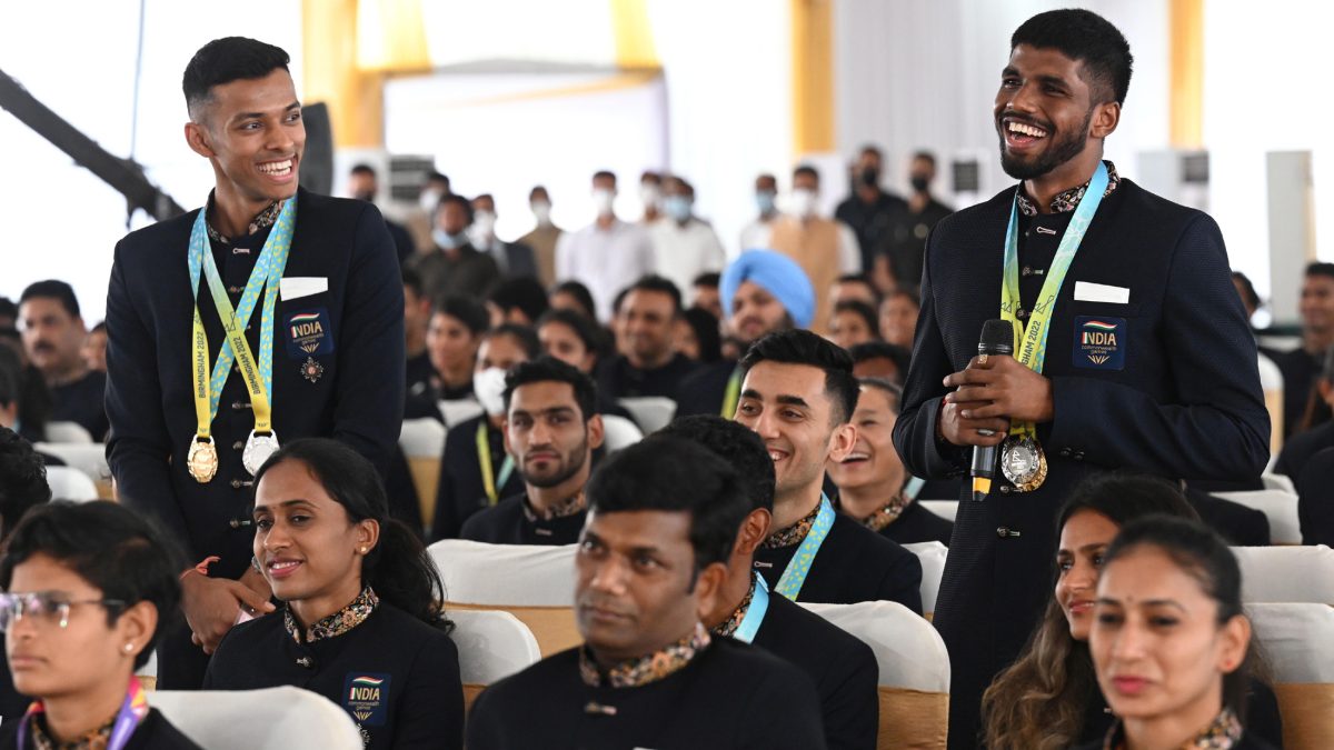 Satwiksairaj Rankireddy and Chirag Shetty standing and smiling with their medals among seated athletes