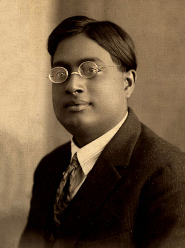 A sepia portrait of a young Satyendra Nath Bose in round glasses and a suit