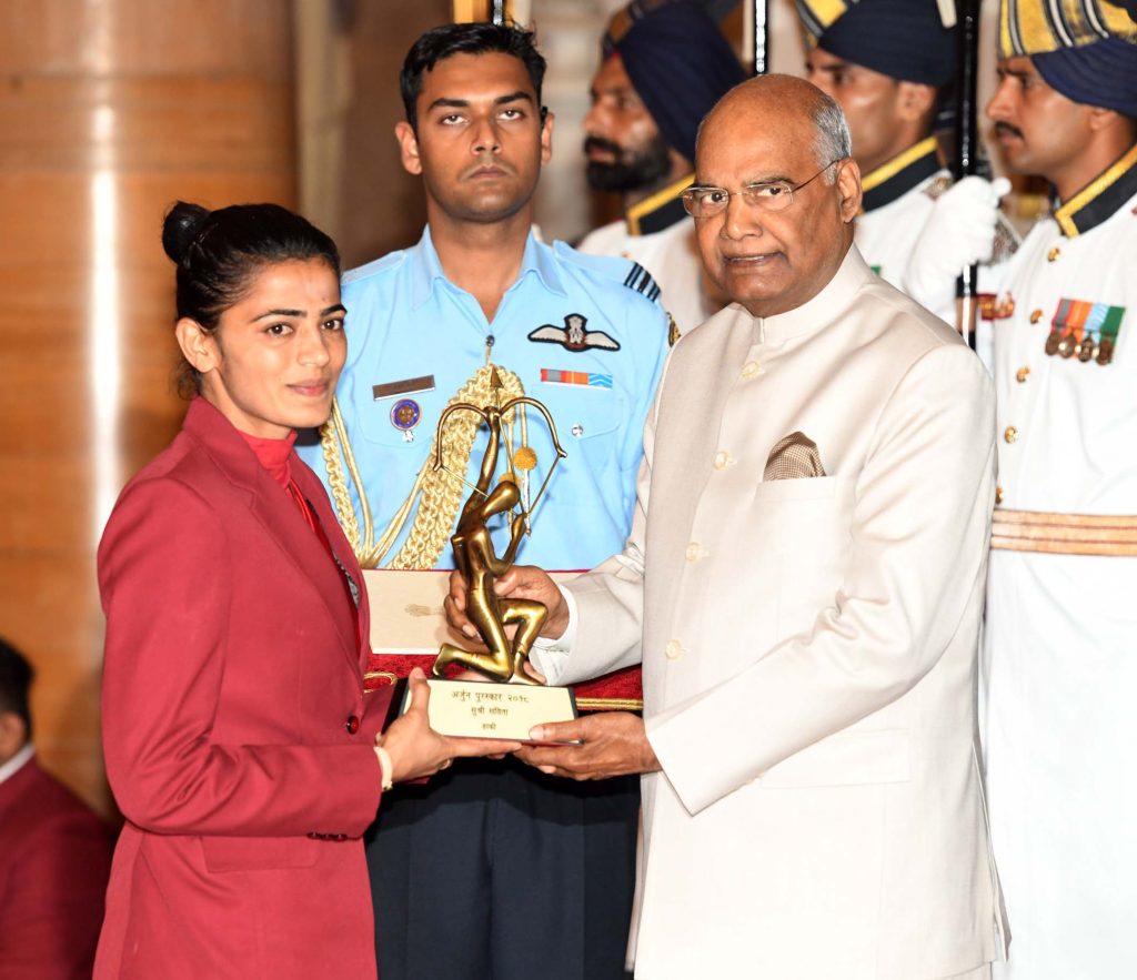 Savita Punia in a maroon blazer receiving the Arjuna Award trophy from President Ram Nath Kovind
