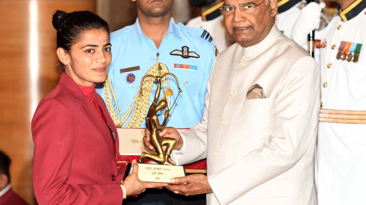 Savita Punia in a maroon blazer receiving the Arjuna Award trophy from President Ram Nath Kovind
